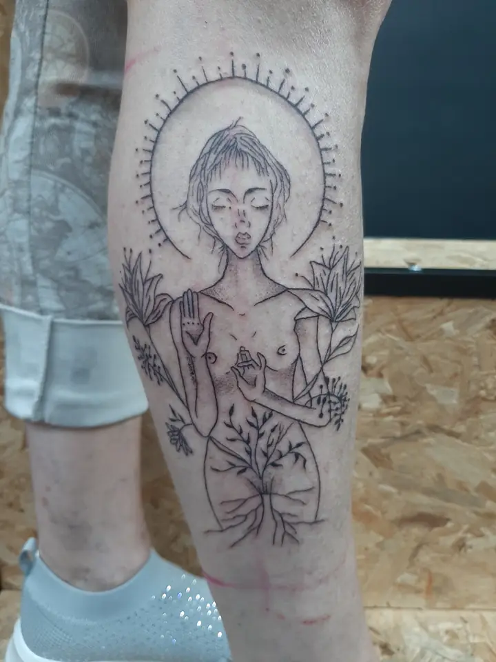 Haloed figure with botanical linework, engraving-style leg tattoo